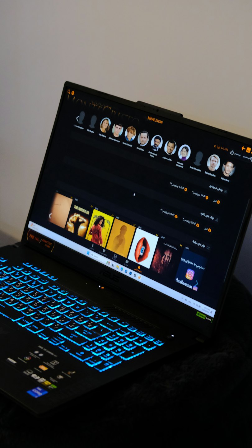 Black laptop displaying a movie streaming interface with blue backlit keys.