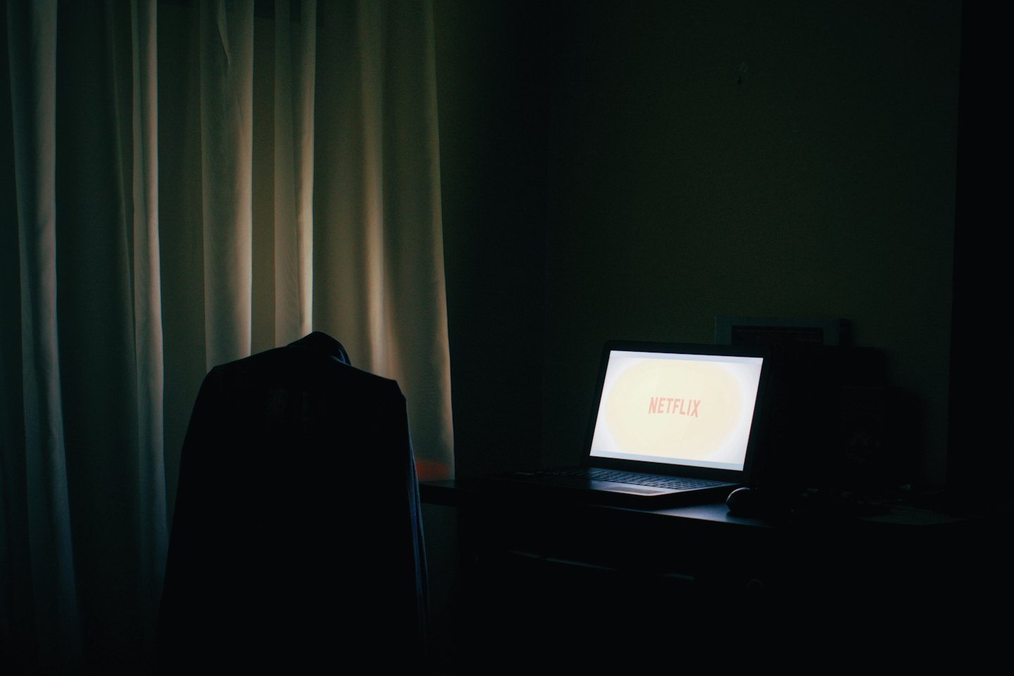 Laptop screen showing the Netflix logo in a dark room.
